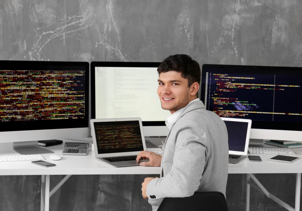 A developer at a multi-monitor workstation showing code and dashboards